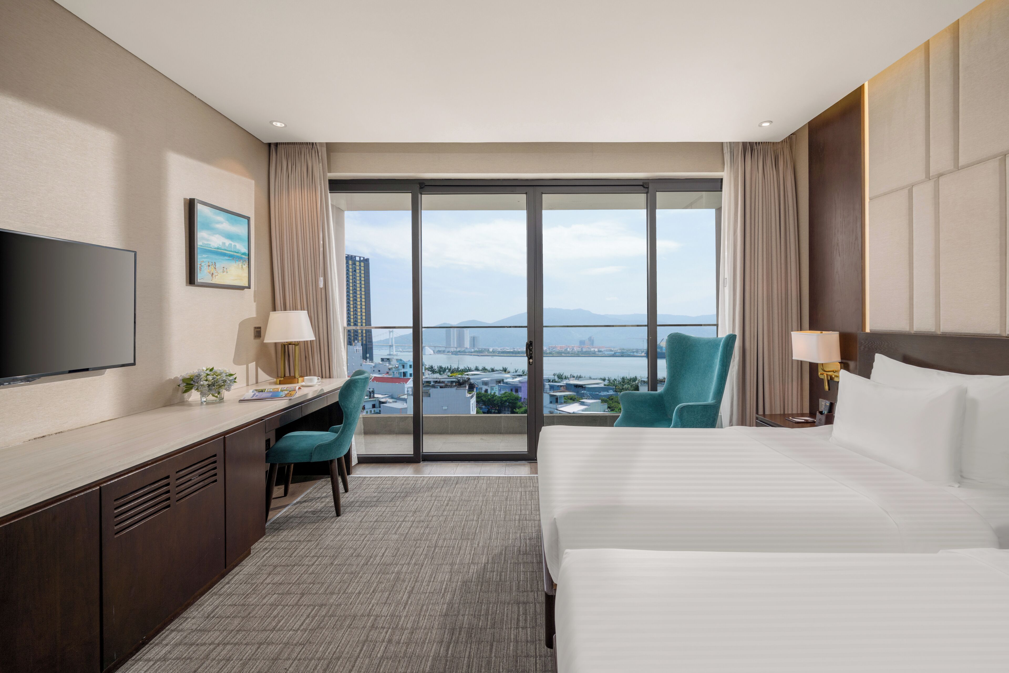 A hotel room with a large bed, a desk with a chair, a television, and a view of a cityscape through a large window.