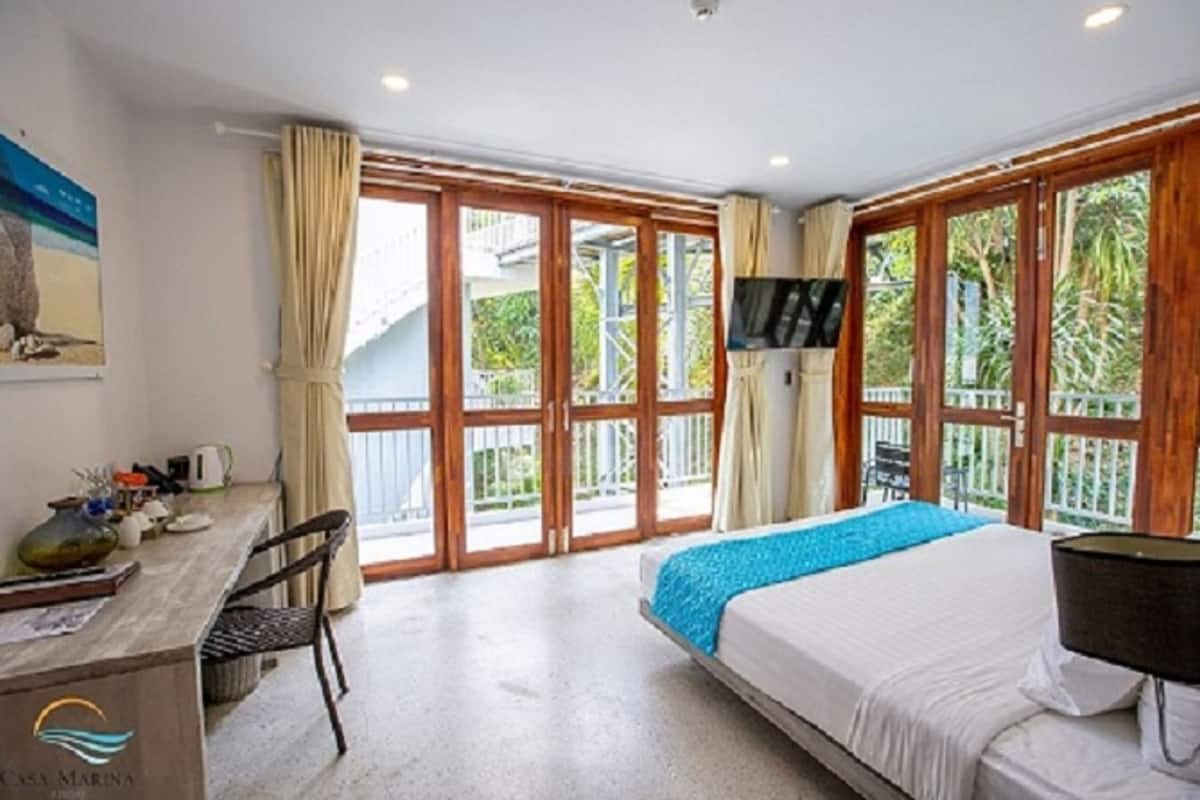 Ein Hotelzimmer mit Bett, Schreibtisch, Sessel, Fernseher und großen Fenstern.
