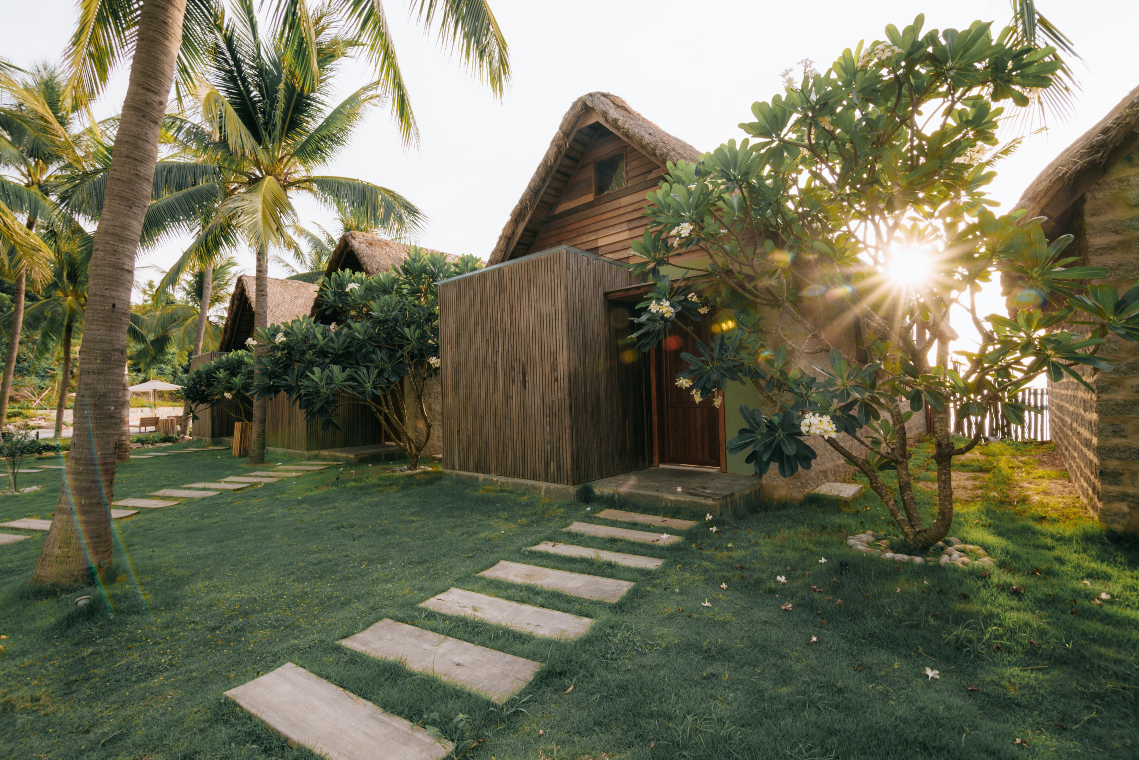 Un complexe hôtelier tropical doté d’un bâtiment à toit de chaume, d’une clôture en bois et d’une pelouse bien entretenue agrémentée de pierres plates servant de marchepied.