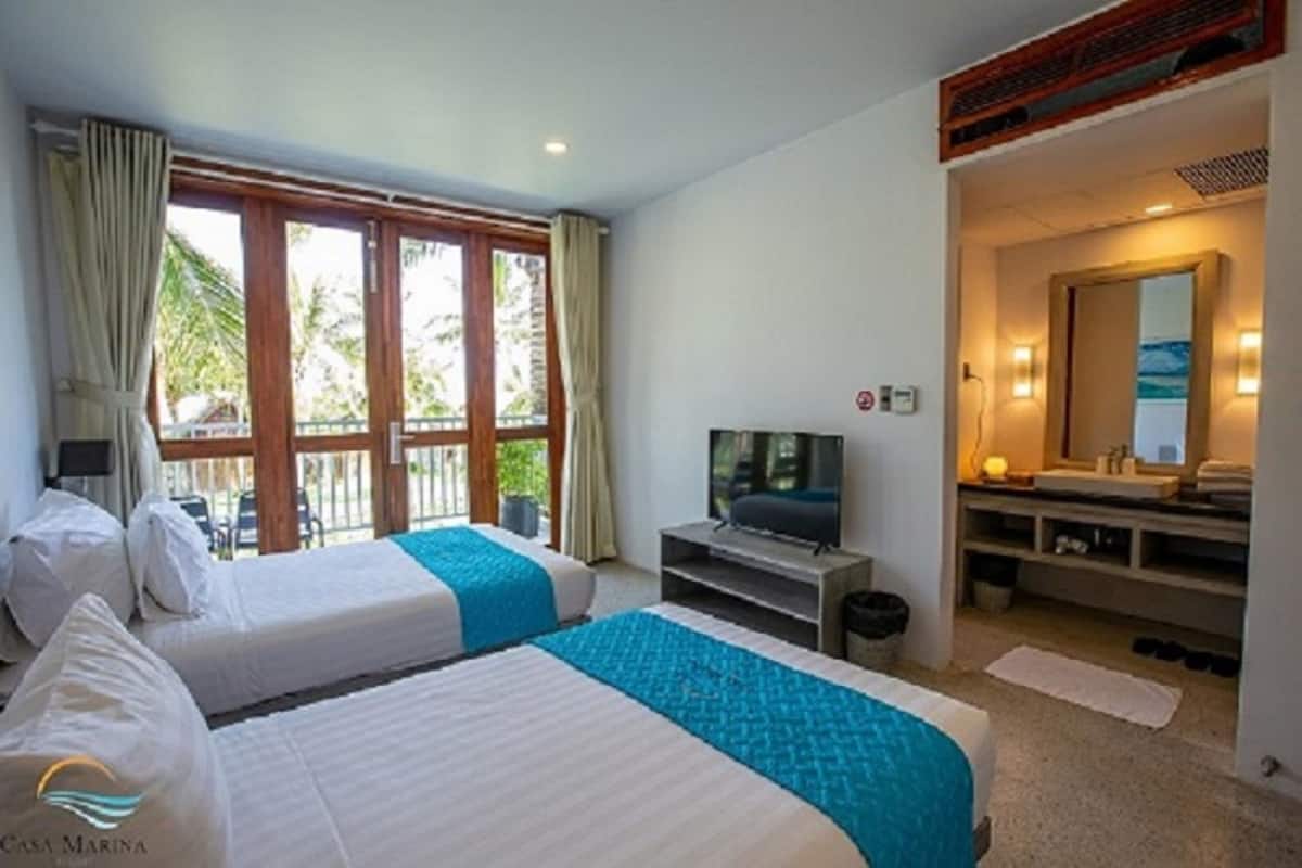 Ein Hotelzimmer mit zwei Betten, einem Fernseher, einem Badezimmer mit Spiegel und Blick ins Freie.