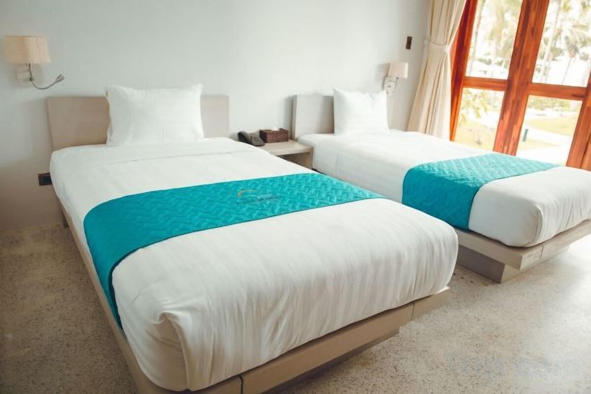 A hotel room with two beds, a nightstand, and a window with curtains.