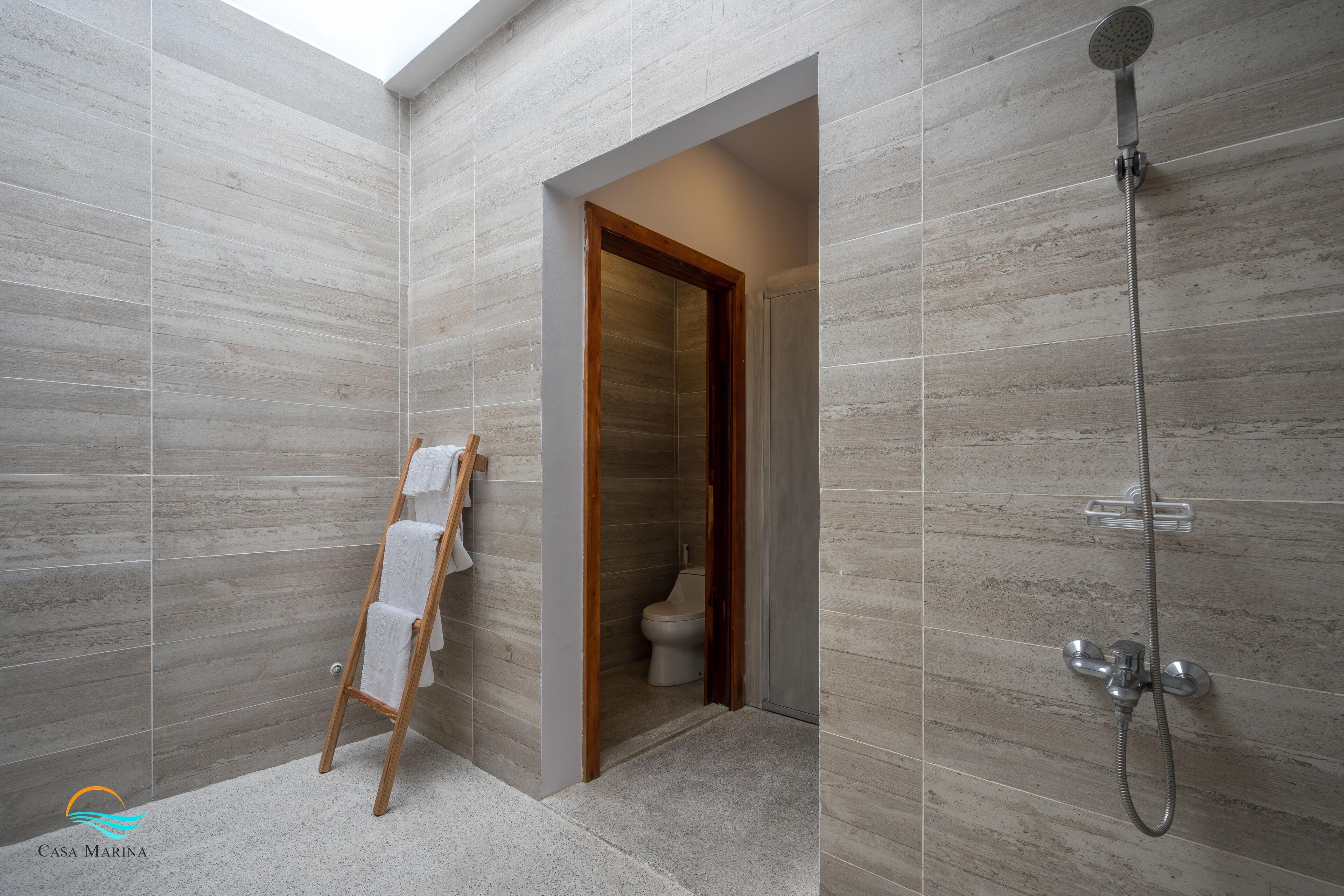 Un baño moderno con ducha, una puerta de madera que da al inodoro y un perchero para toallas.