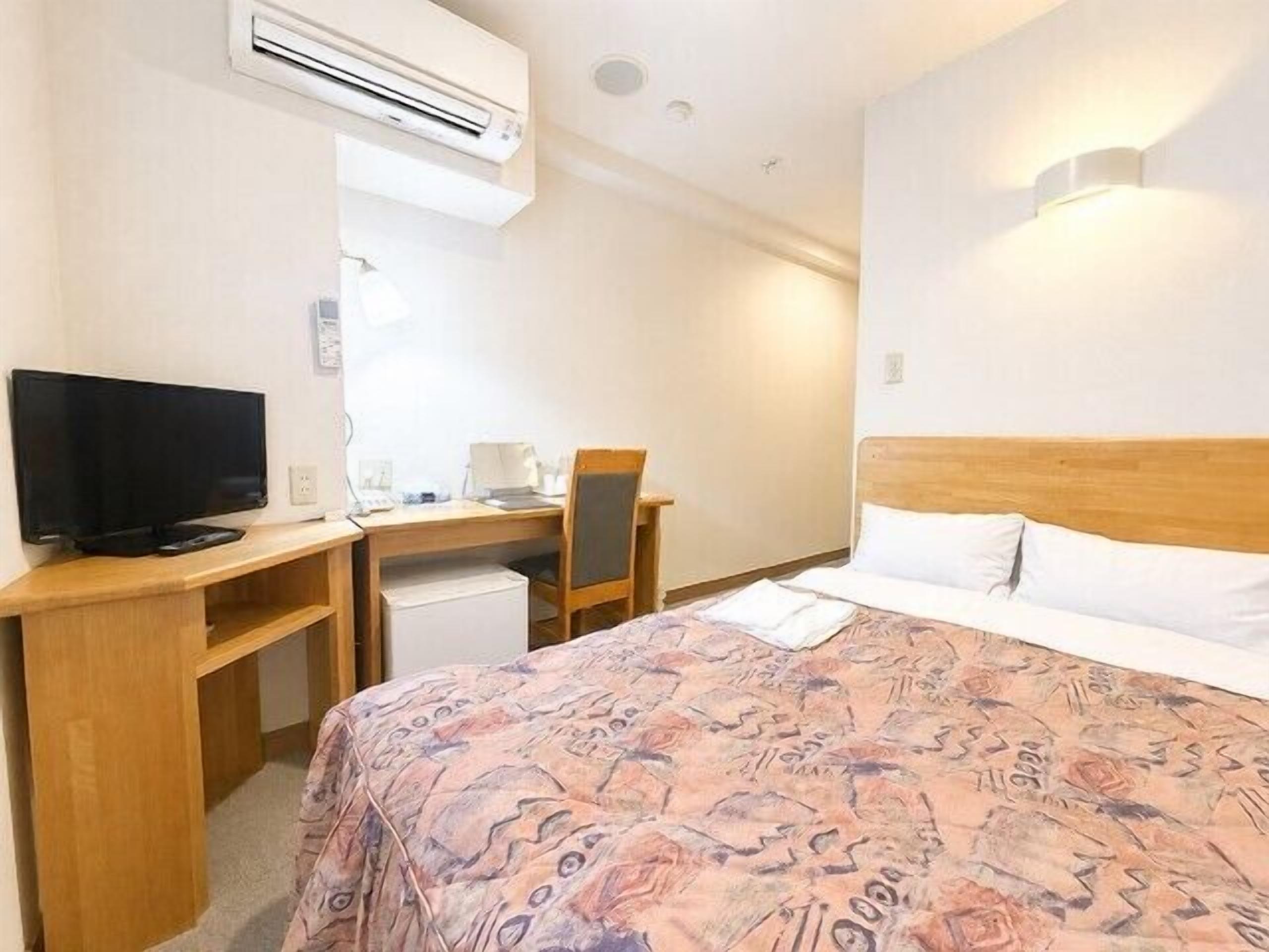 Een hotelkamer met een bed, een bureau met een computer, een televisie en een airconditioning.