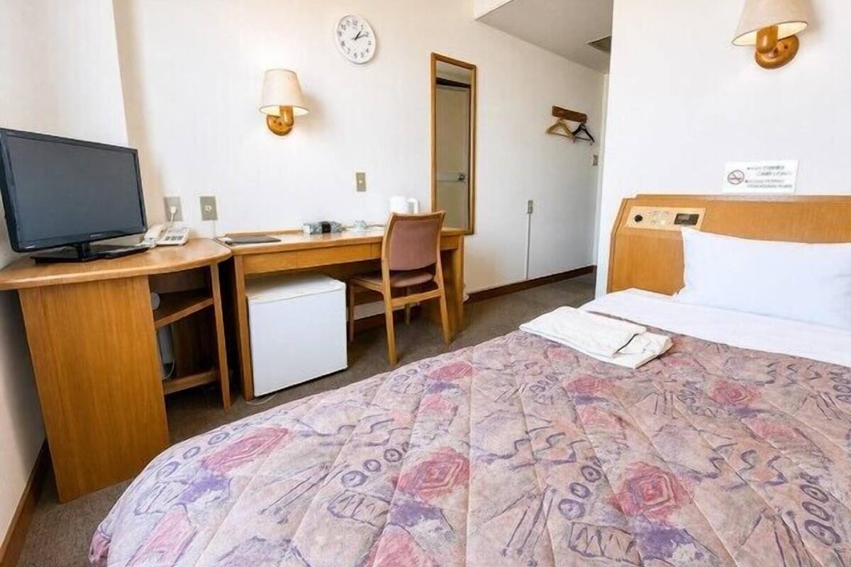 Une chambre d’hôtel équipée d’un lit, d’un bureau, d’une chaise, d’une télévision et d’une horloge murale.