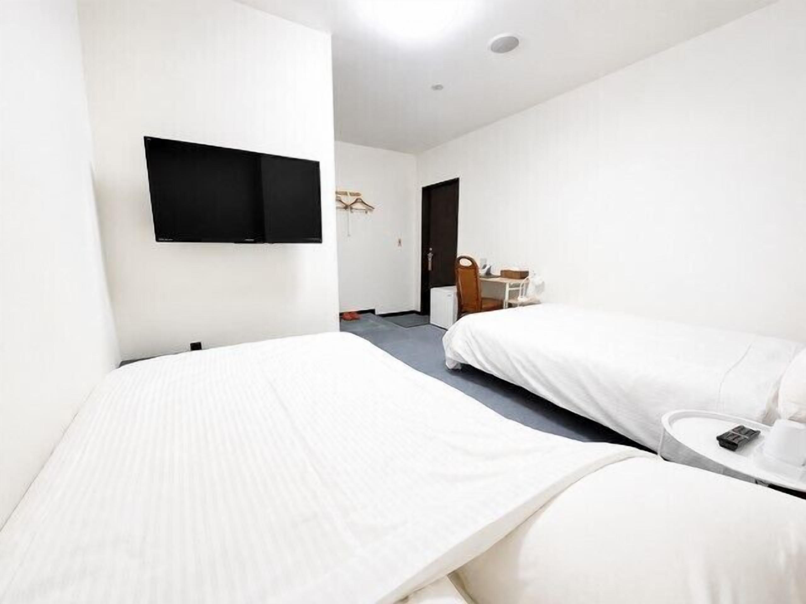 Een hotelkamer met twee bedden, een flatscreen-tv, een bureau met stoel, en een tafeltje met een kopje en telefoon.