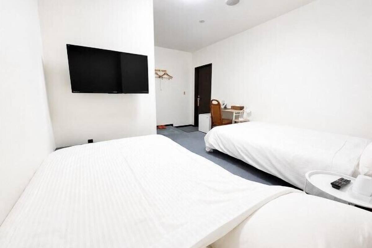 Une chambre d’hôtel avec deux lits, un téléviseur à écran plat, un bureau avec une chaise et une petite table avec une tasse et un téléphone.