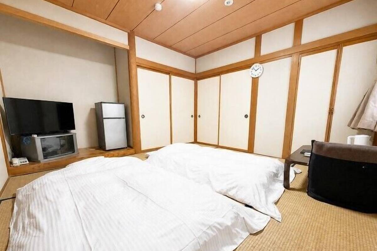 Une chambre avec un lit, une télévision, un réfrigérateur et une horloge au mur.