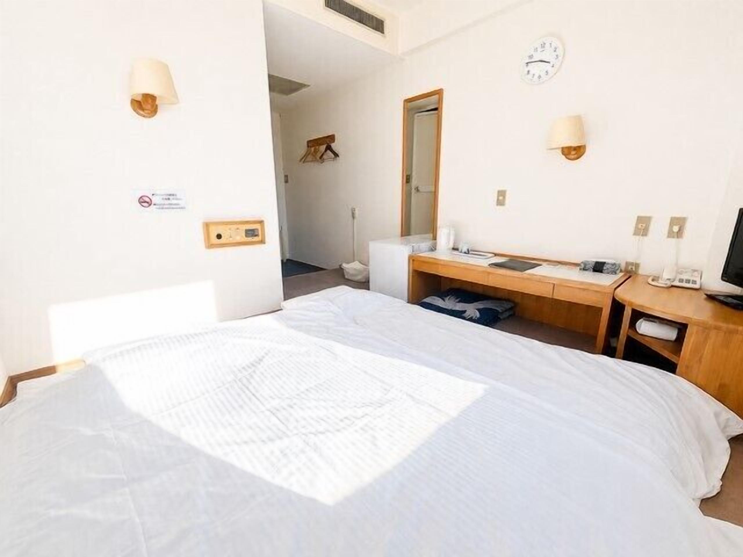 Een hotelkamer met een bed, een bureau, een stoel, een televisie en een klok aan de muur.