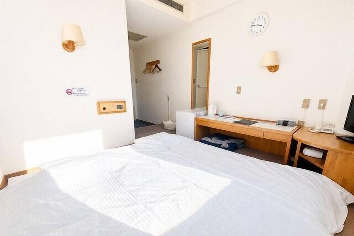 Une chambre d’hôtel avec un lit, un bureau, une chaise, une télévision et une horloge au mur.