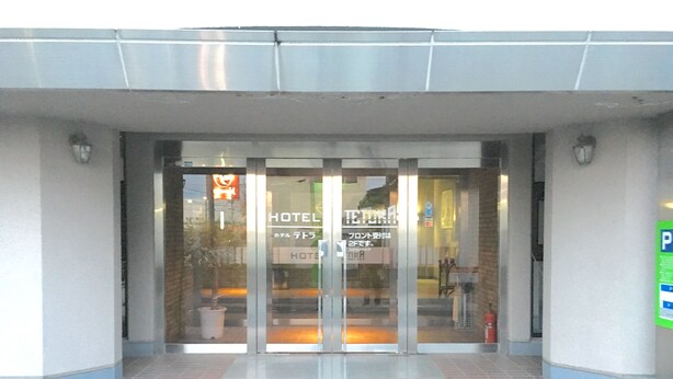 A hotel entrance with a glass door, a fire hydrant outside, and a parking sign to the right.