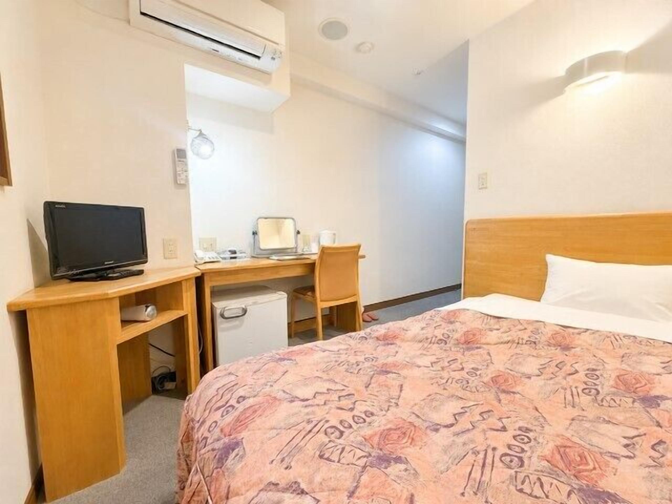 Een hotelkamer met een bed, een bureau met een computer, een televisie en een airconditioning.