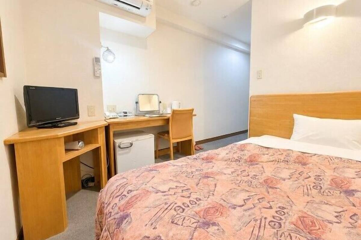 Une chambre d’hôtel équipée d’un lit, d’un bureau avec un ordinateur, d’une télévision et d’un appareil de climatisation.