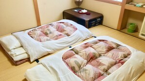 Two beds with floral bedding, a small table with a scale, and a trash bin.