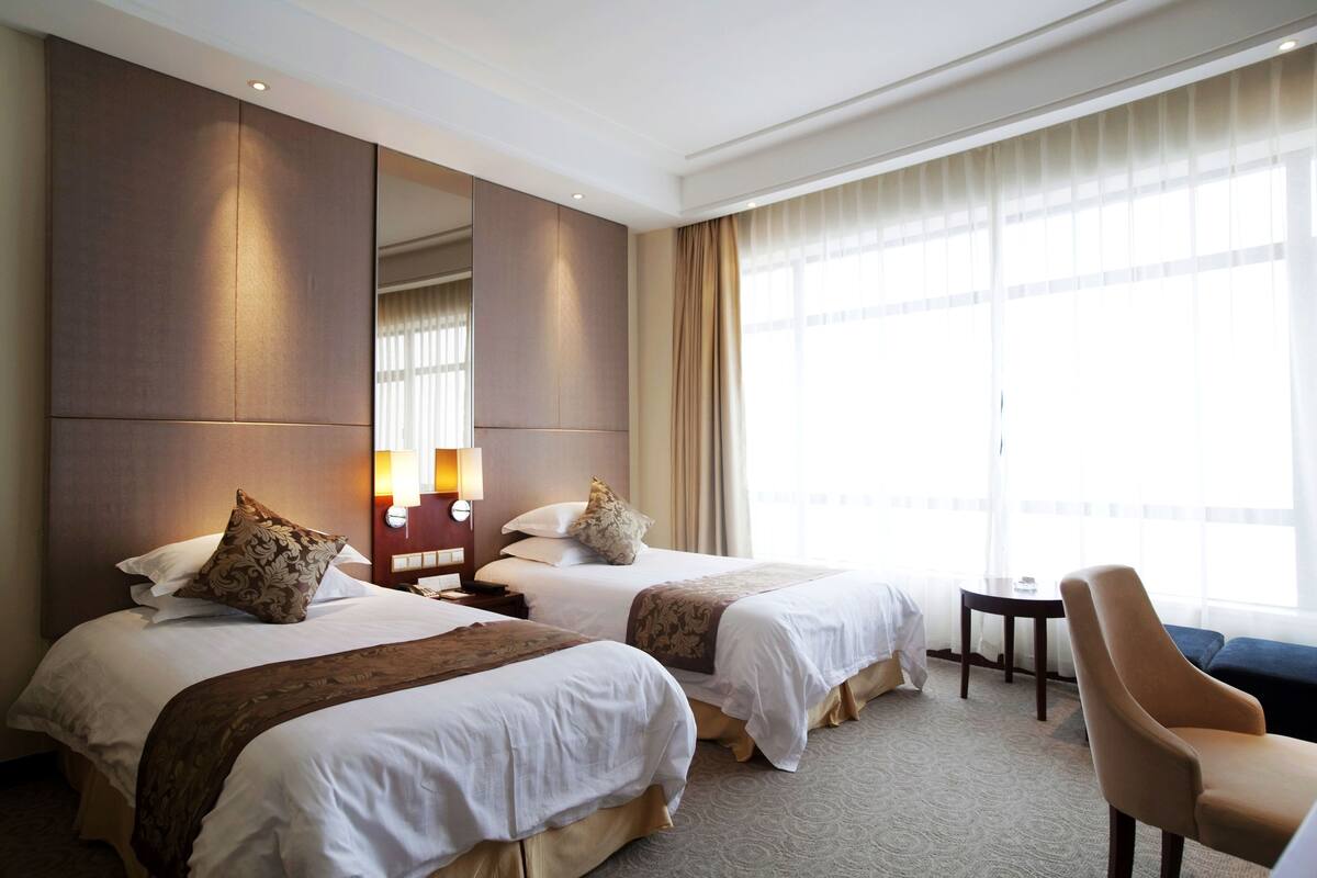 A hotel room with two beds, a large mirror, a small table, and a chair.