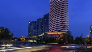 A modern hotel with a curved facade, multiple floors, and illuminated windows. - Longting New Century Hotel Qiandao Lake (Hangzhou)