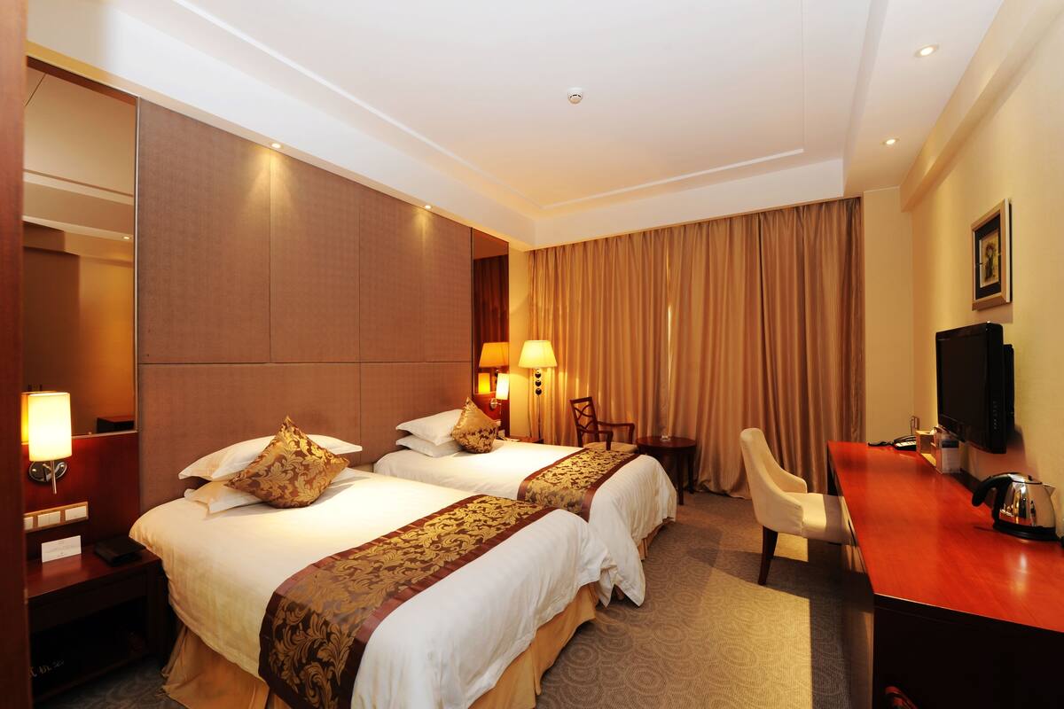 A hotel room with two beds, a desk, a chair, a television, and a mirror.