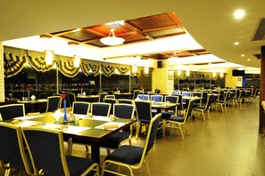 Un restaurante espacioso con numerosas mesas y sillas, techo alto con vigas de madera y elementos decorativos colgantes.