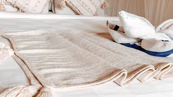 A neatly made bed with a beige blanket and pillows, a blue and beige throw blanket, and a white canopy.