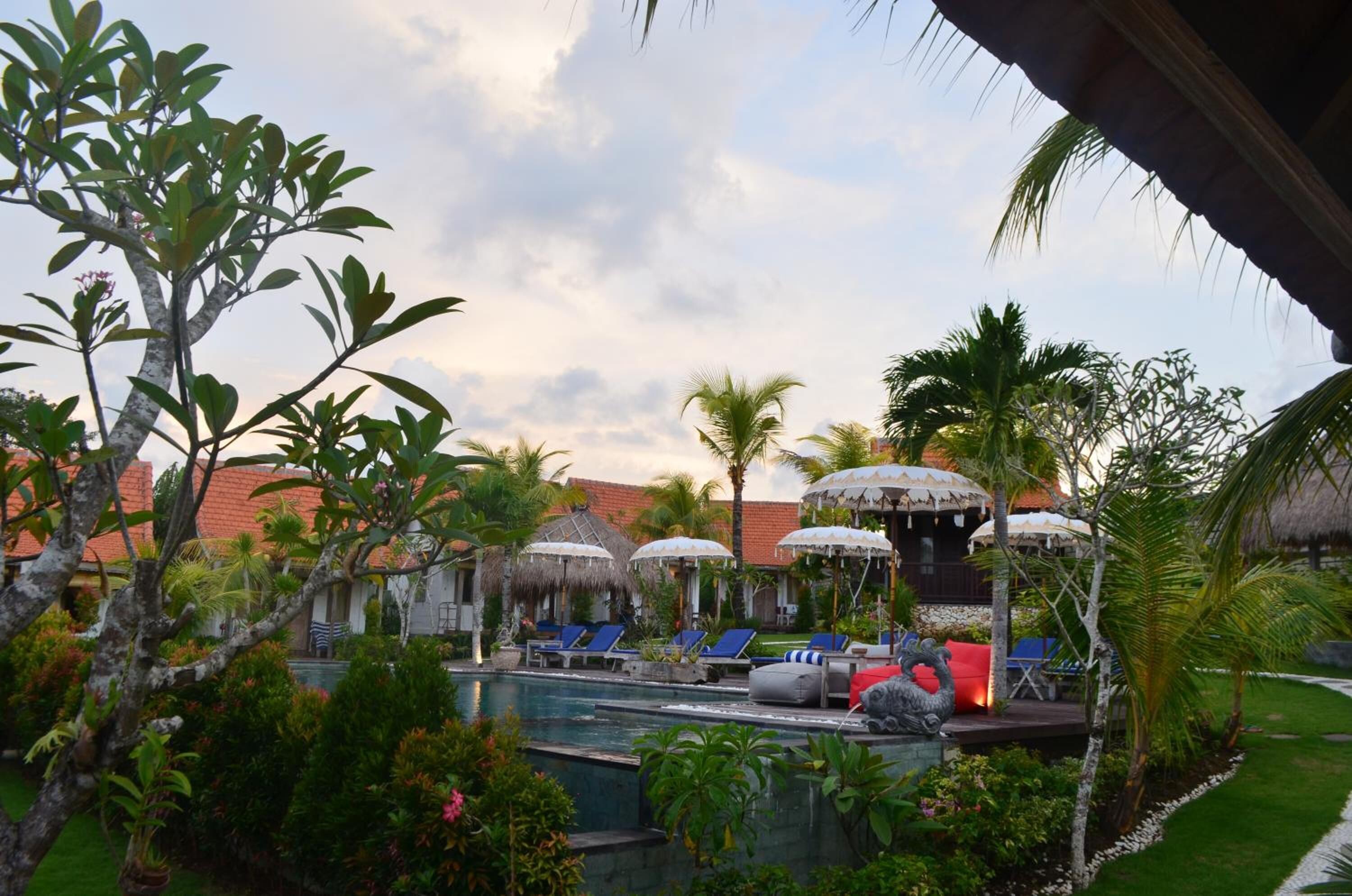 Uma área à beira da piscina com espreguiçadeiras, guarda-sóis e uma estrutura com telhado de palha.