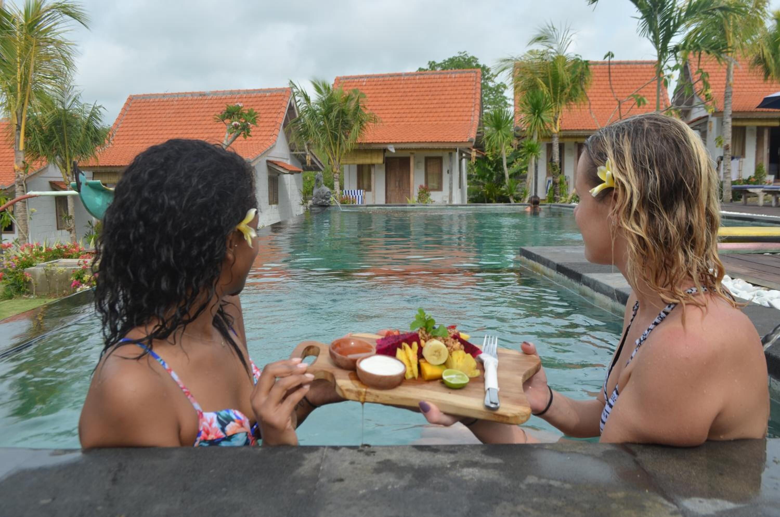 Dos personas en una piscina sosteniendo una bandeja con comida y bebidas.