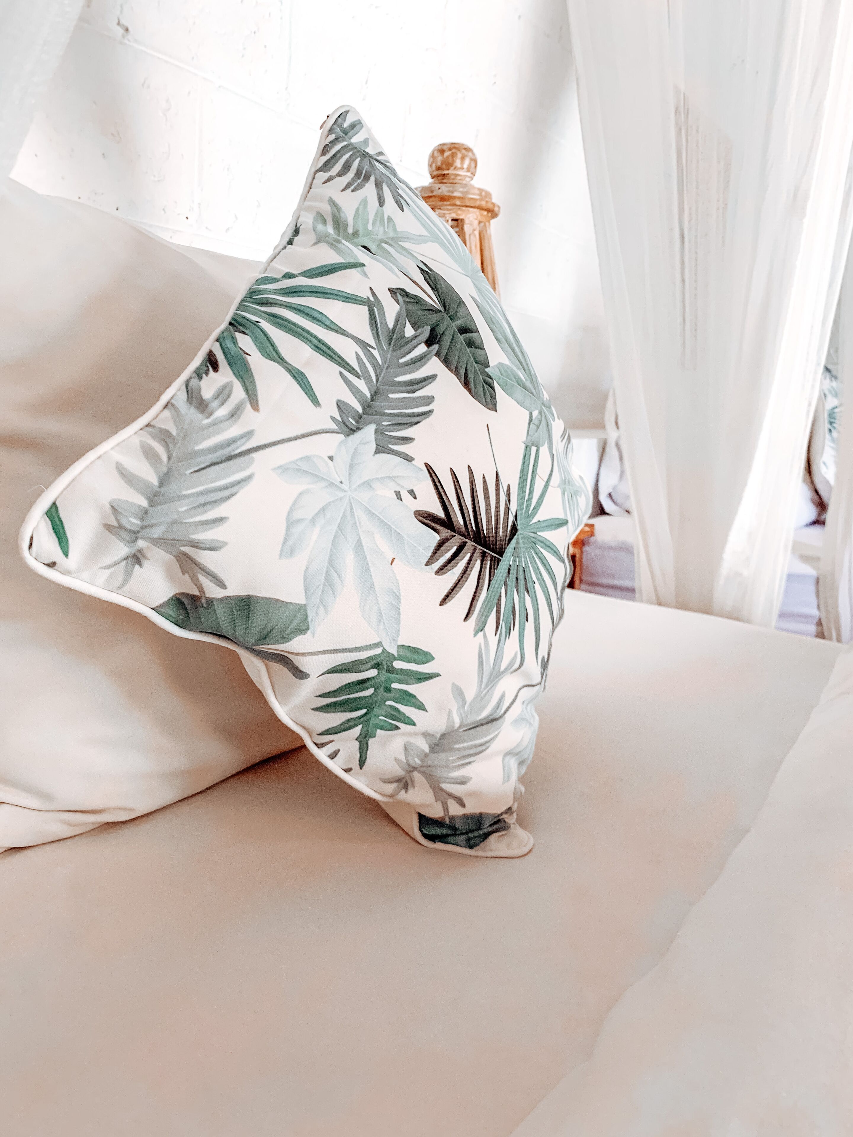 Un almohadón con estampado de hojas tropicales sobre una cama.
