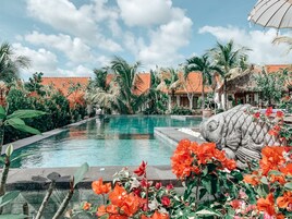 A swimming pool surrounded by tropical plants and palm trees, with a clear sky above.