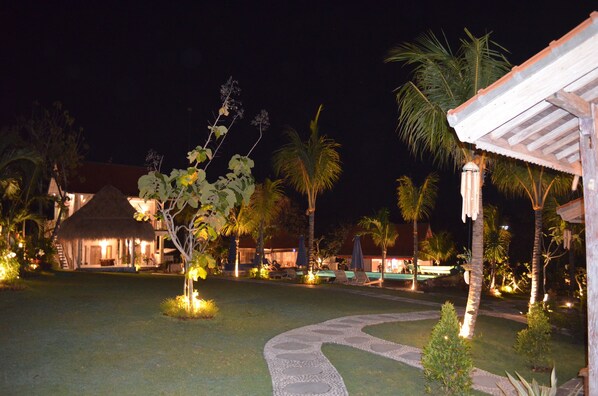 A nighttime resort with a thatched-roof building, palm trees, and a well-lit pathway. - Uluwatu Breeze Village (Pecatu)
