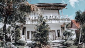 A two-story building with a balcony, surrounded by tropical plants and a stone pathway. - Uluwatu Breeze Village (Pecatu)