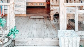 A rustic wooden cabin with a bed under a canopy, a small table, and a potted plant. - Uluwatu Breeze Village (Pecatu)