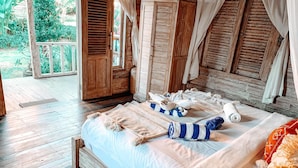 A wooden bed with white linens, a wooden wardrobe, and a view of the garden through open shutters. - Uluwatu Breeze Village (Pecatu)