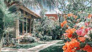 A garden pathway leading to a building with a tiled roof, surrounded by lush greenery and flowering plants. - Uluwatu Breeze Village (Pecatu)