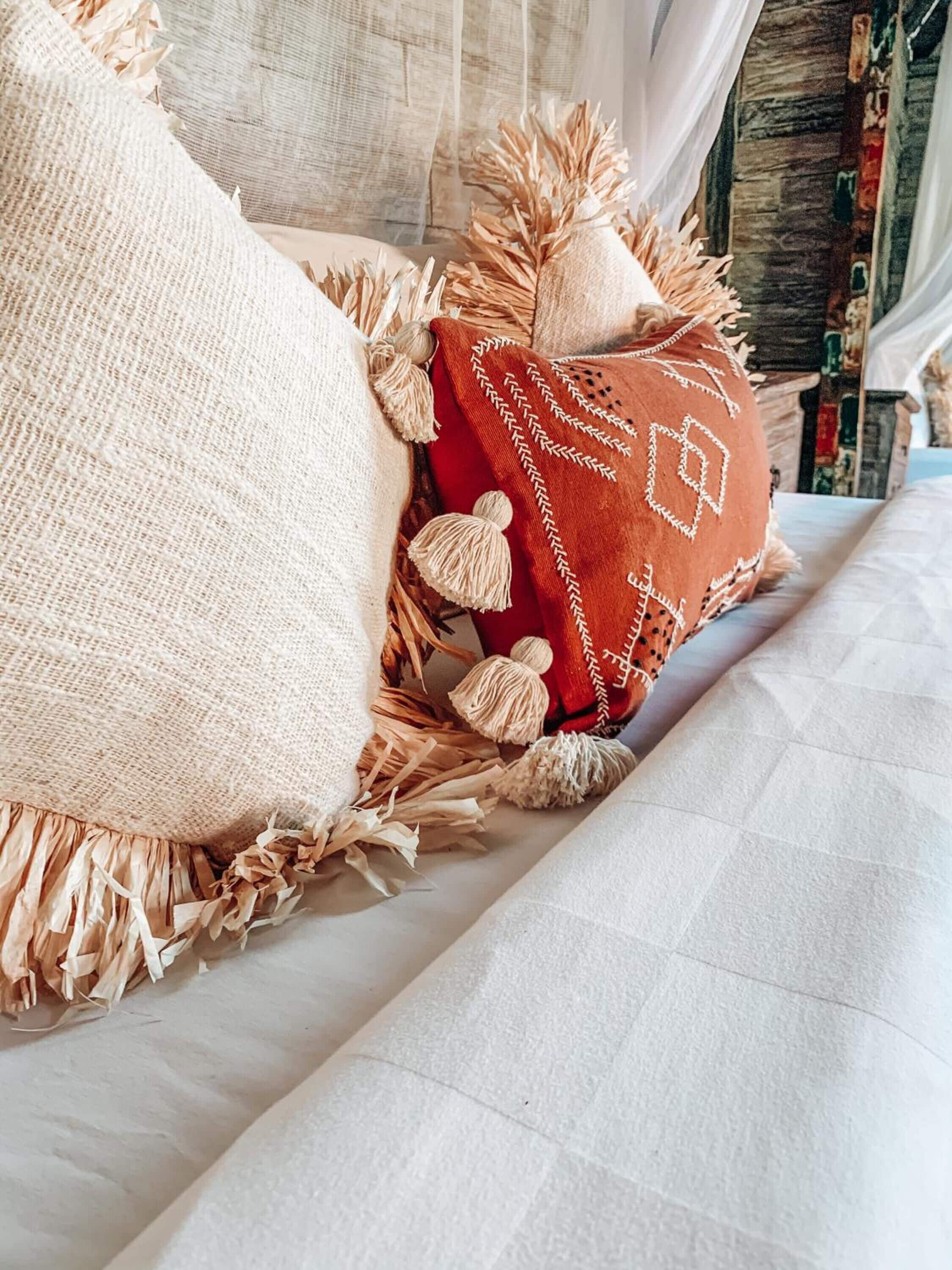 Un lit recouvert d’une couverture blanche à texture et agrémenté d’un coussin rouge orné de glands.