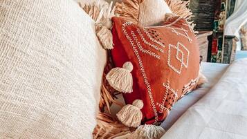 Un lit recouvert d’une couverture blanche à texture et agrémenté d’un coussin rouge orné de glands.