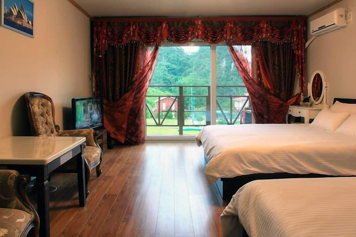 A hotel room with two beds, a desk, a chair, a television, and a balcony with curtains.