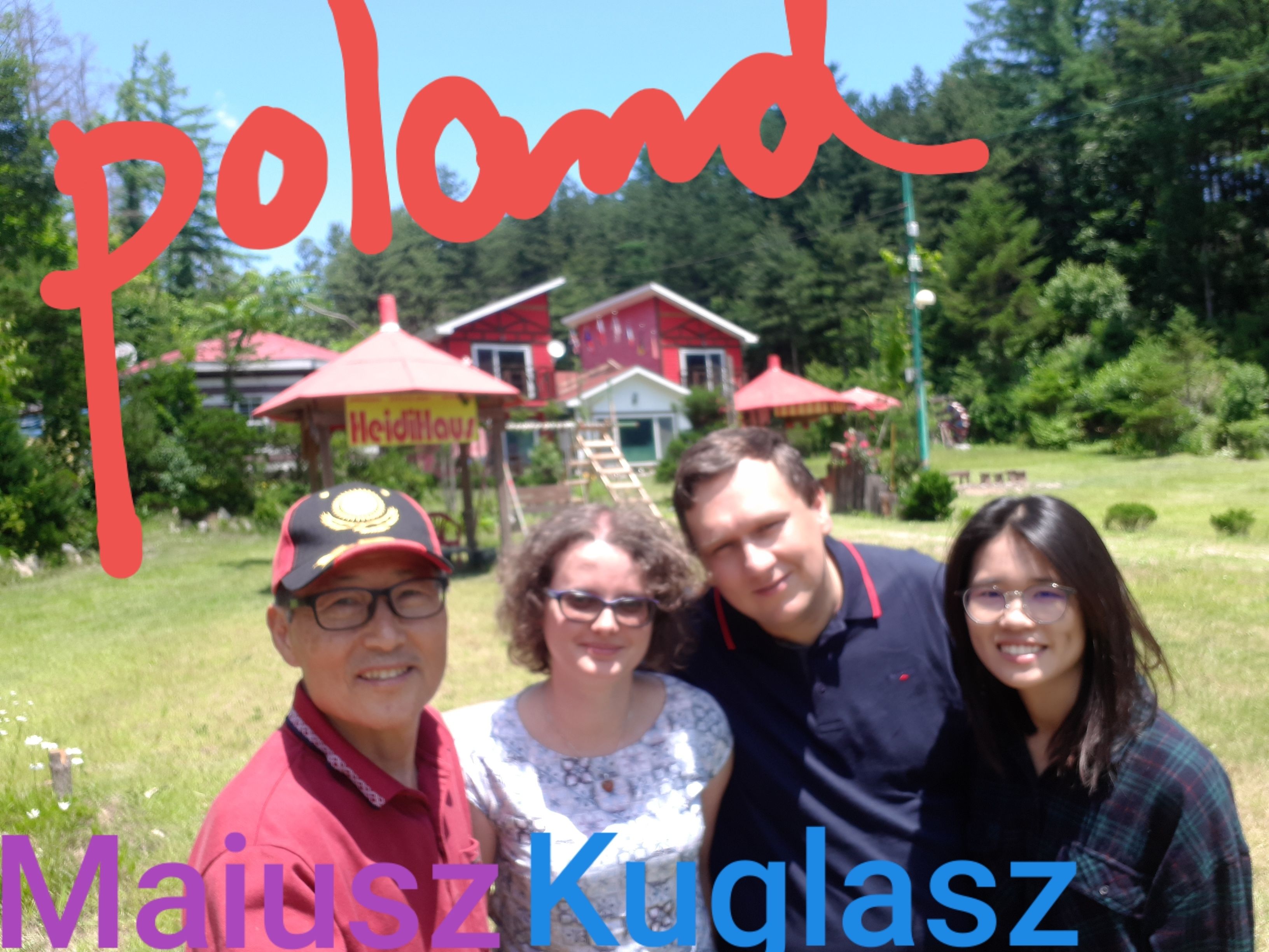 A group of people in a garden with a red house and umbrellas in the background.