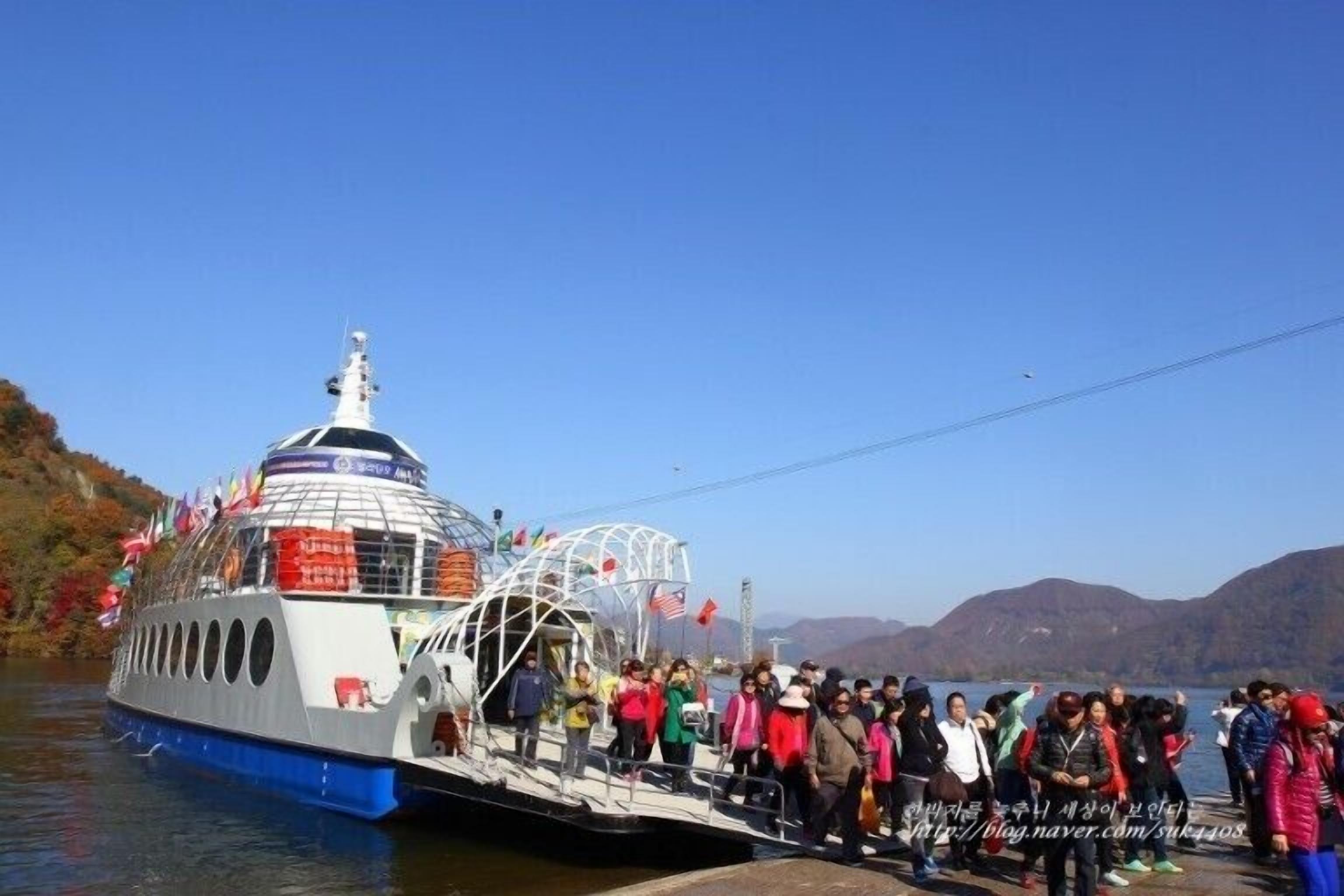 A boat with a covered deck and multiple windows, docked at a pier with a group of people standing on the side.