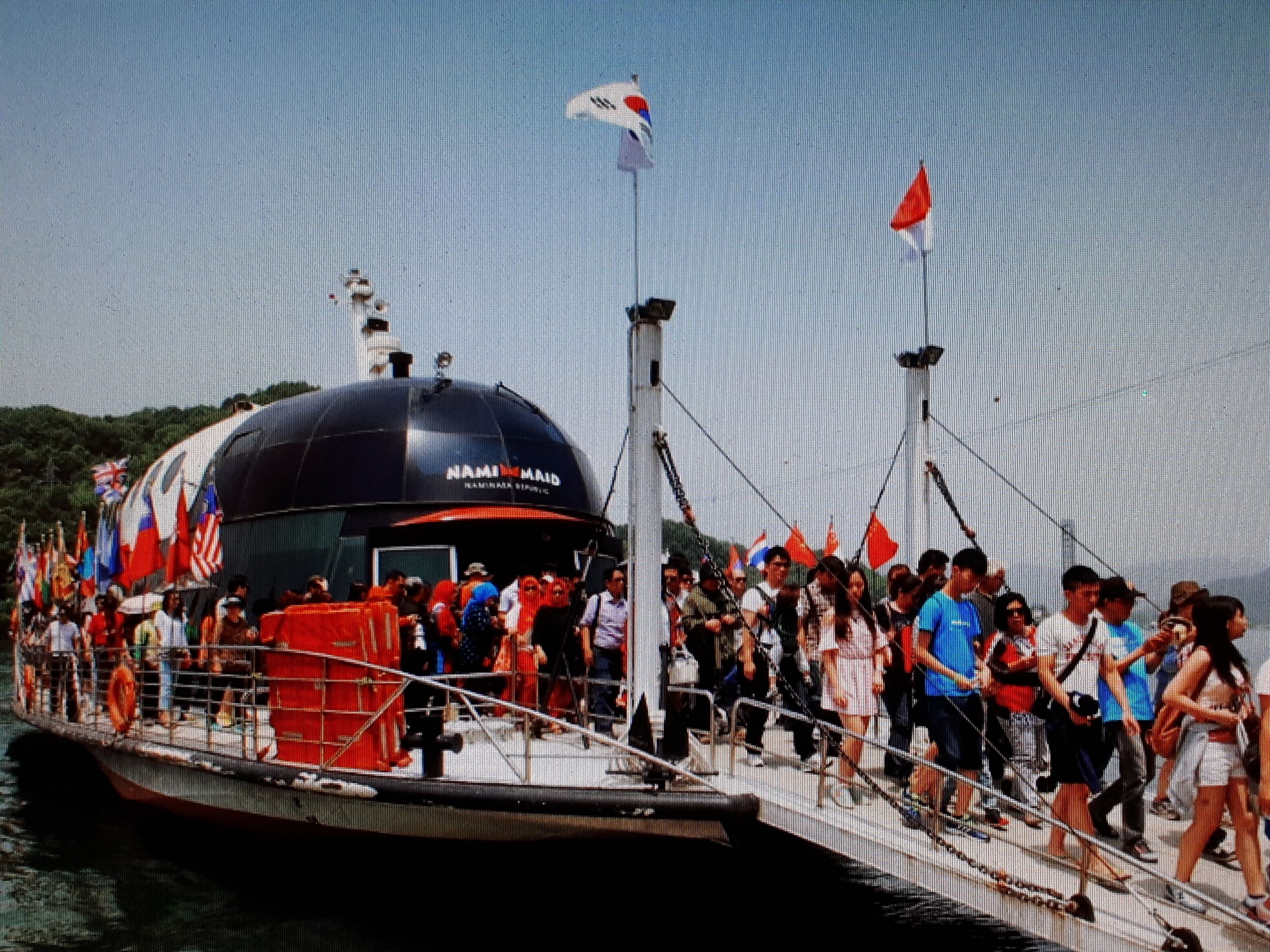 A large boat with a dome structure, surrounded by people and flags.