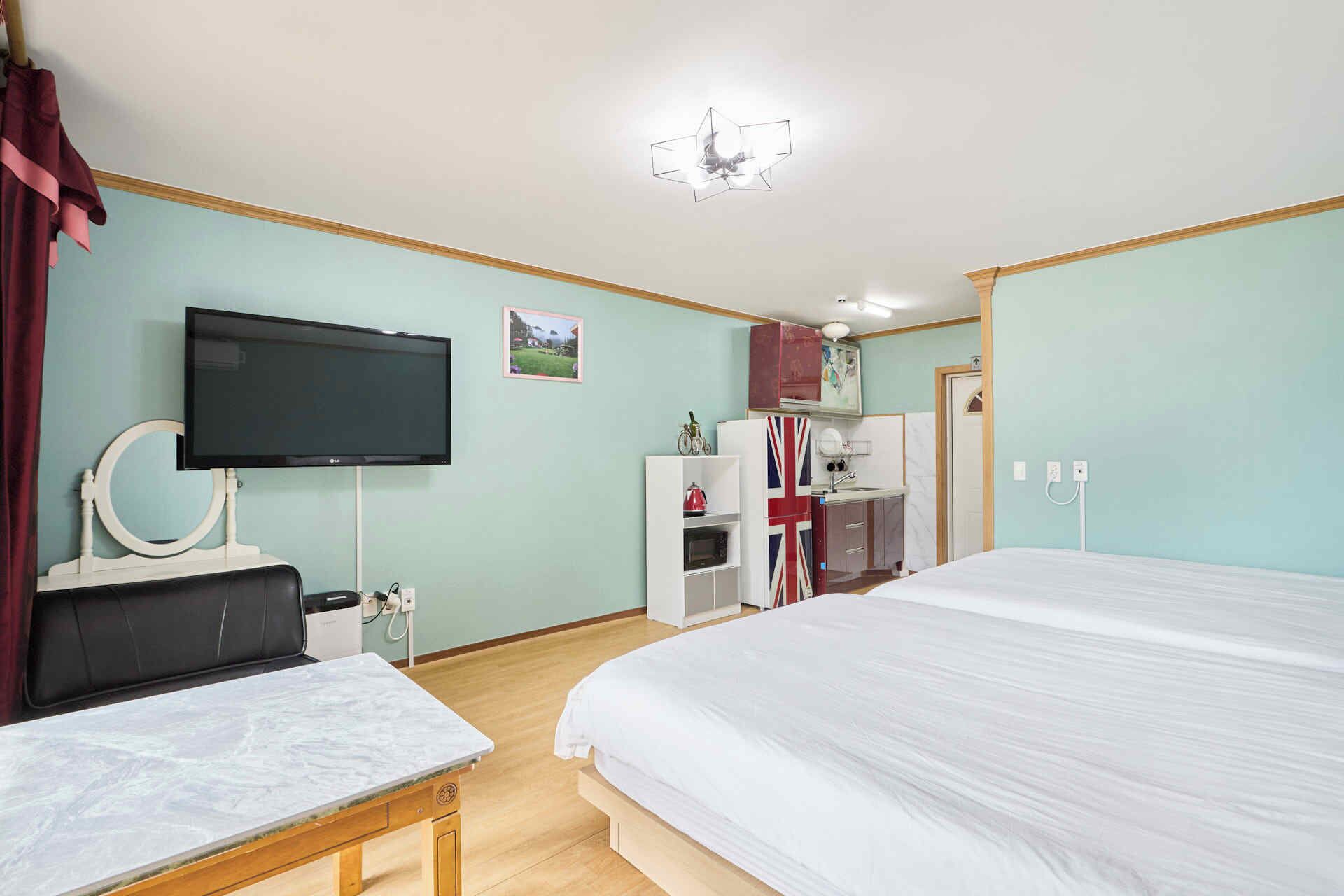 A hotel room with a bed, a TV, a desk, a mirror, a wardrobe, and a kitchenette.