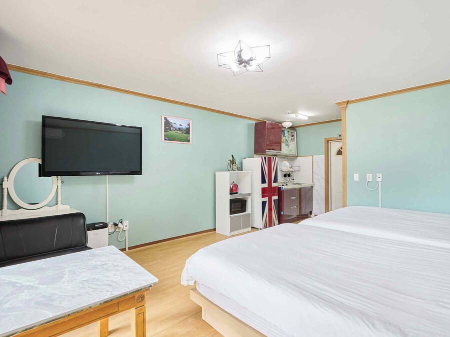 A hotel room with a bed, a TV, a desk, a mirror, a wardrobe, and a kitchenette.