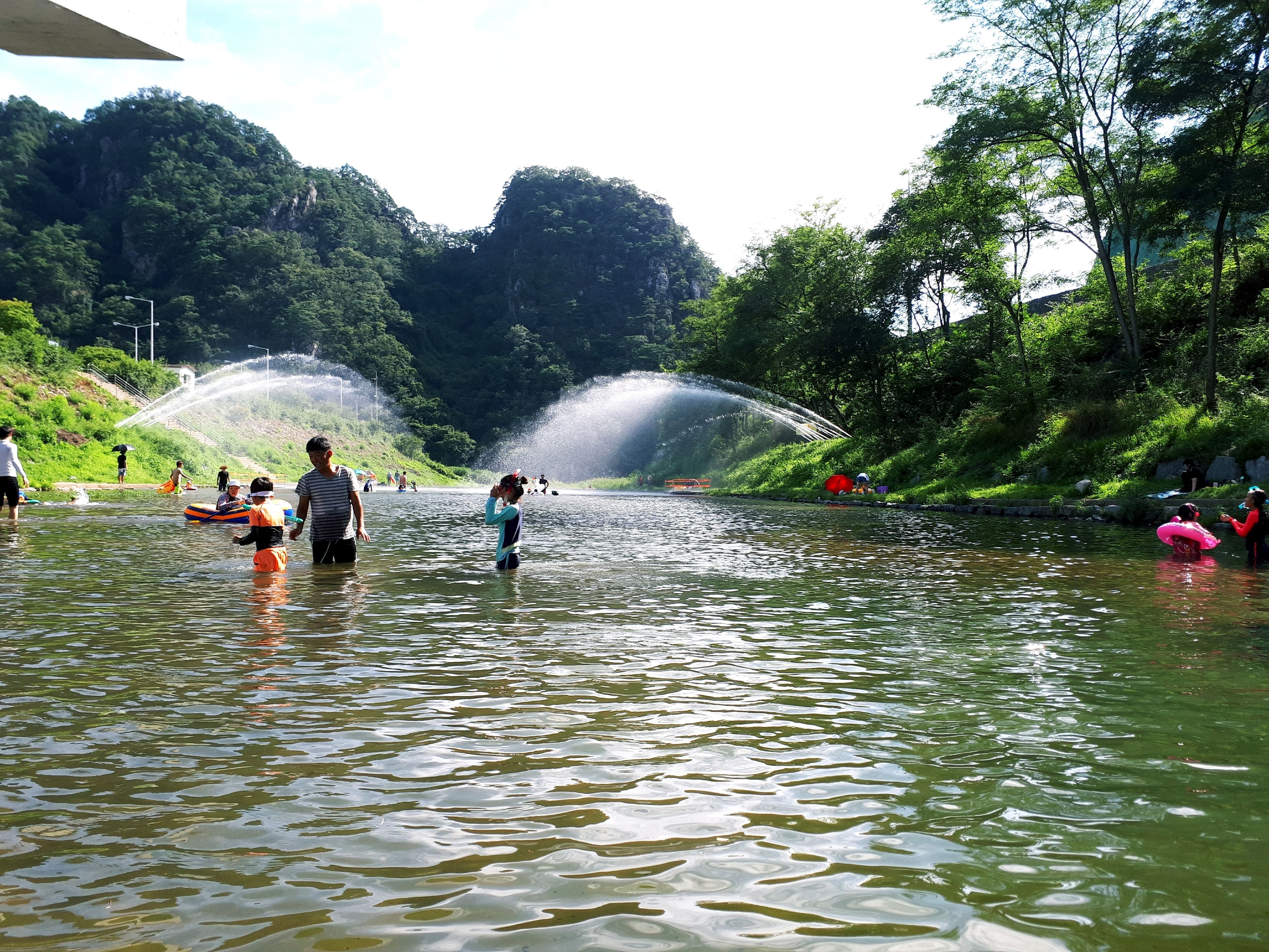 A river with people engaging in water activities, surrounded by lush greenery and hills.