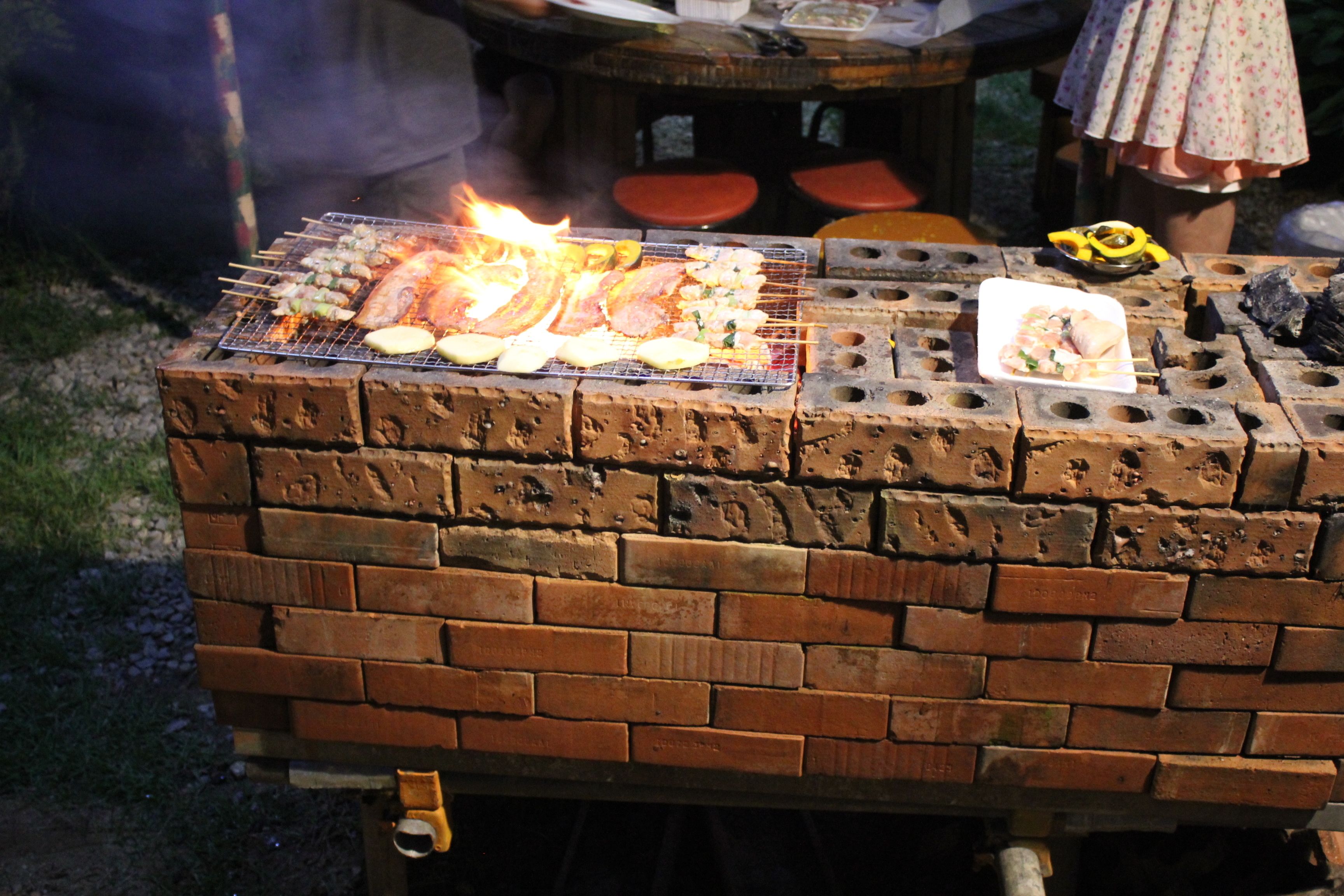 Ein Backsteingrill mit Fleisch- und Gemüserspießen, einem Teller Essen und einer Flasche.
