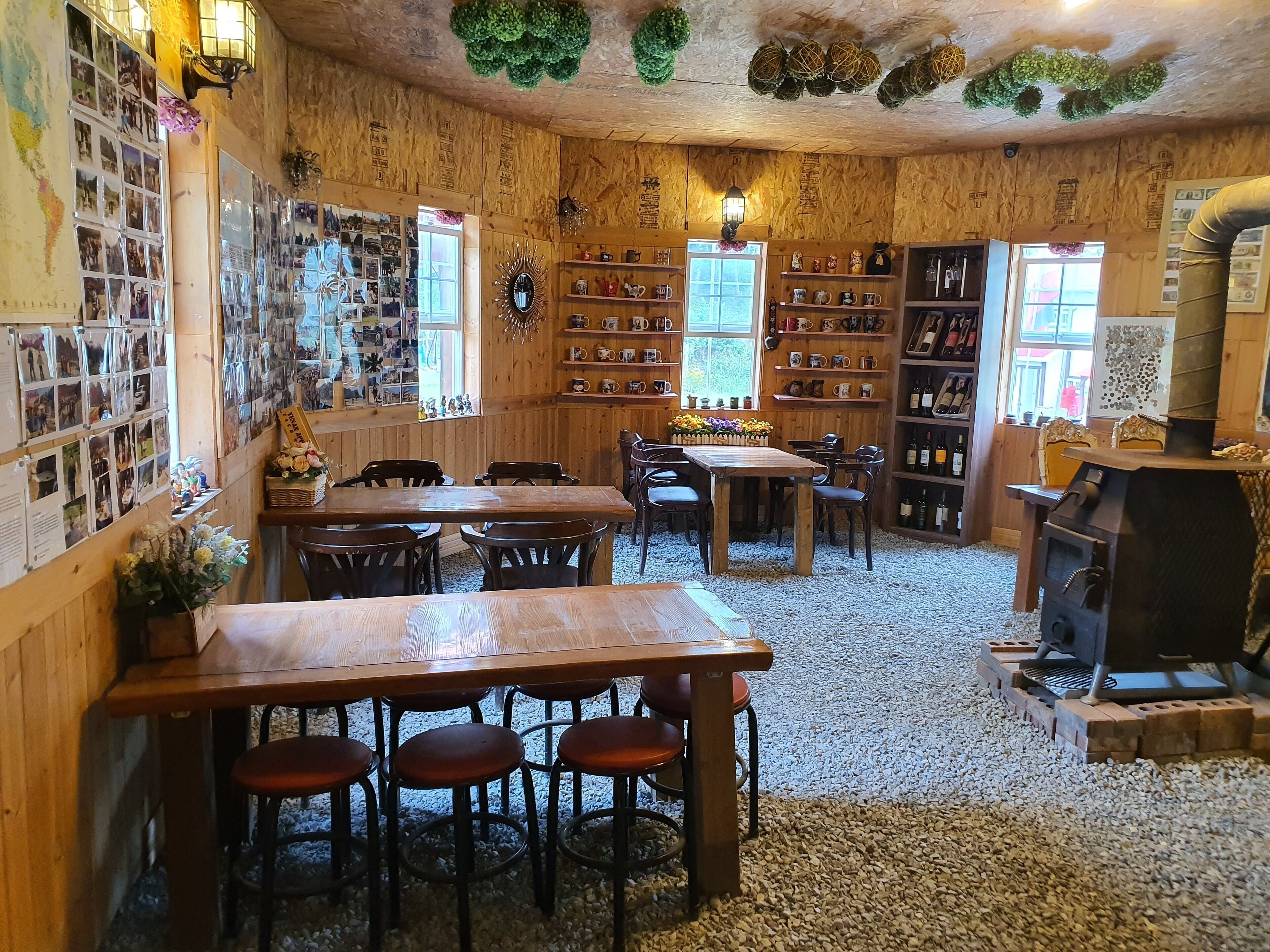 A cozy room with wooden walls, a wooden table with chairs, shelves with mugs, and a fireplace.