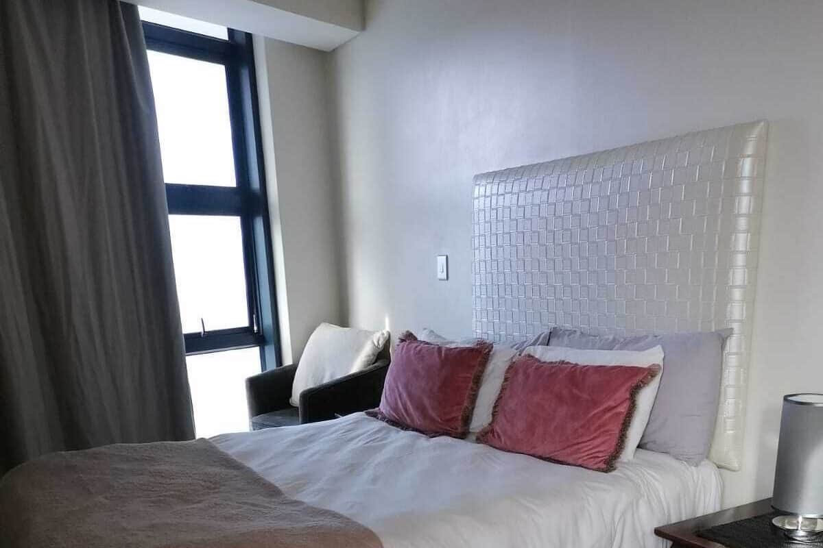 Une chambre bien rangée, avec un grand lit, une table de chevet et une fenêtre avec des rideaux.