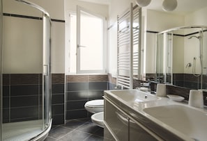 A modern bathroom with a glass shower enclosure, a toilet, and a sink with a mirror. - UR-NEST Clavature - Piazza Maggiore Collection (Bologna)