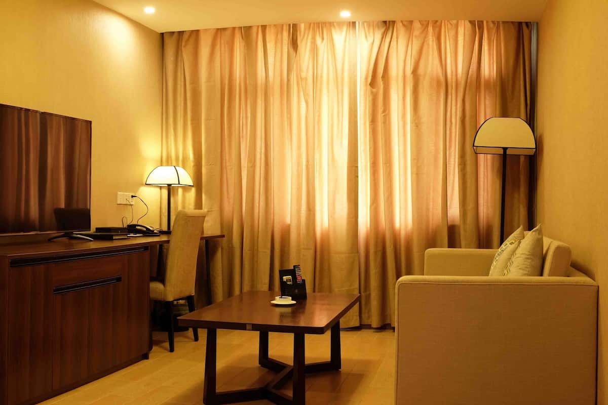 A hotel room with a wooden desk, a television, a lamp, a sofa, and a curtain.