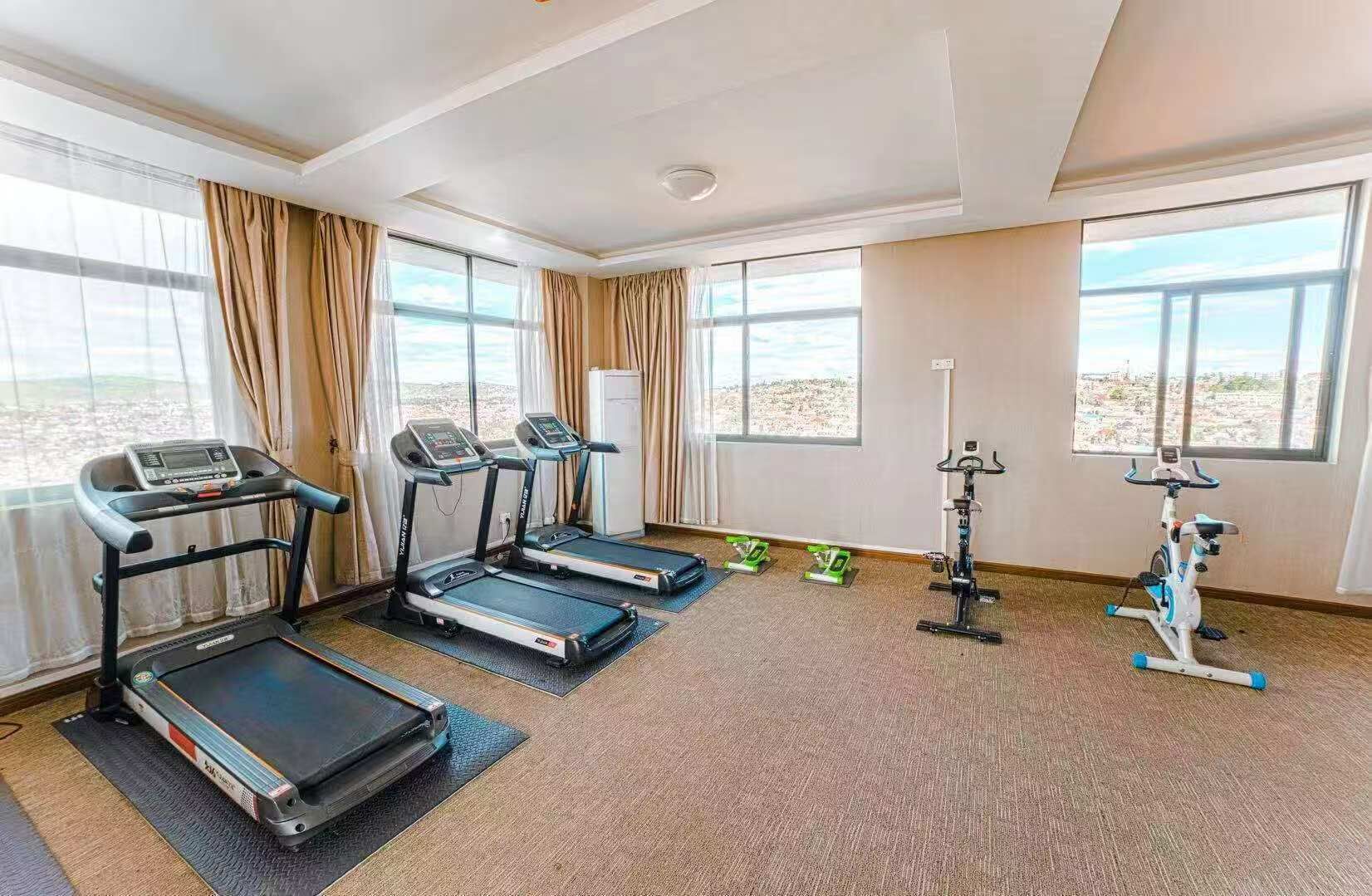 A hotel room with a treadmill, elliptical, stationary bike, and weights.