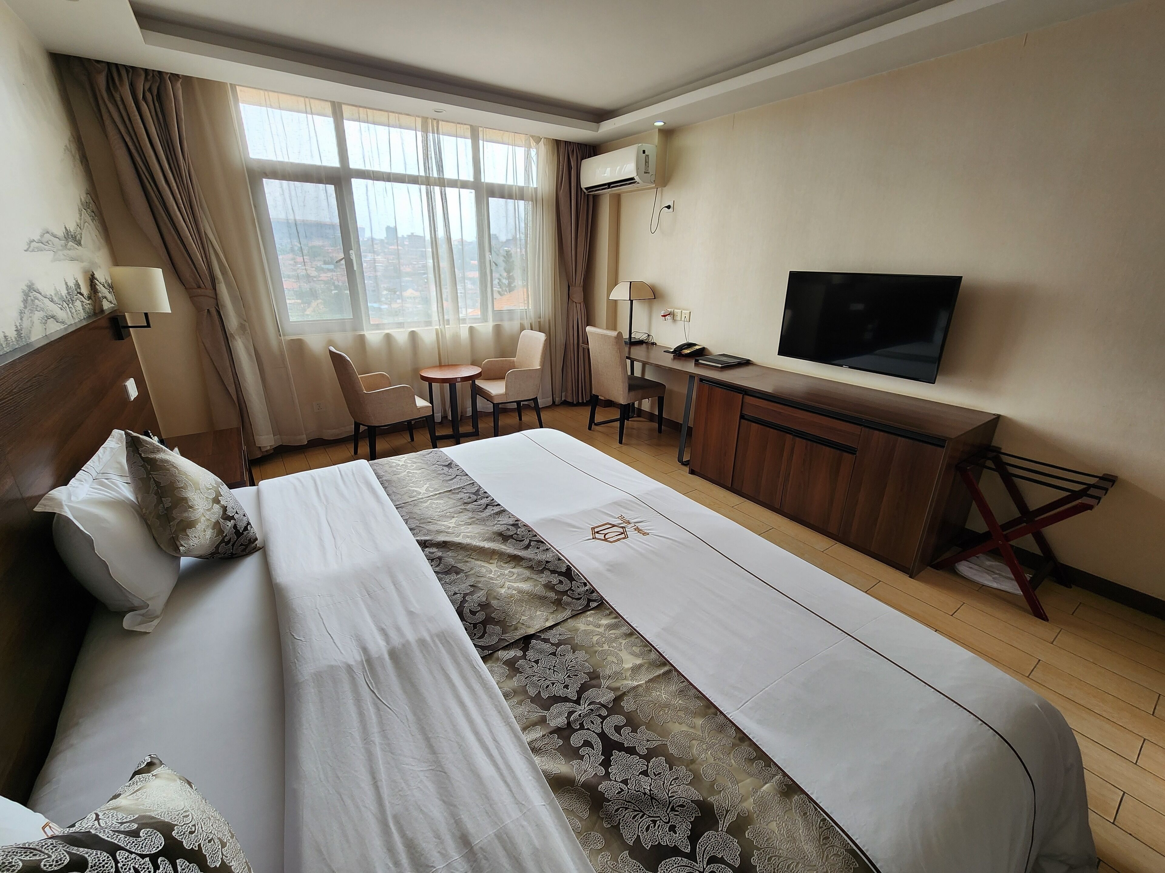 Una habitación de hotel con una cama grande, un escritorio, una silla, un televisor y un ventanal con cortinas.