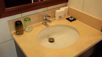 A bathroom sink with a mirror above it, a towel dispenser, and two bottles on the counter.