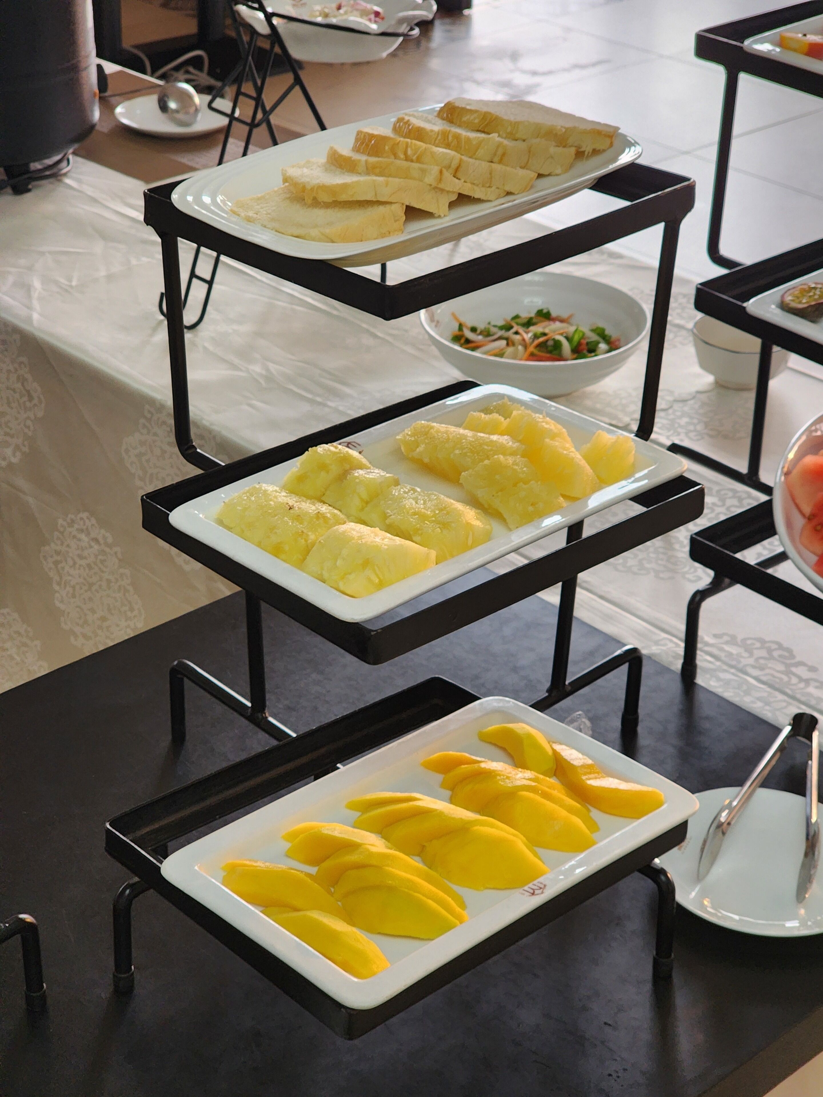 A buffet setup with various food items on trays, including bread, pineapple, and mango slices.