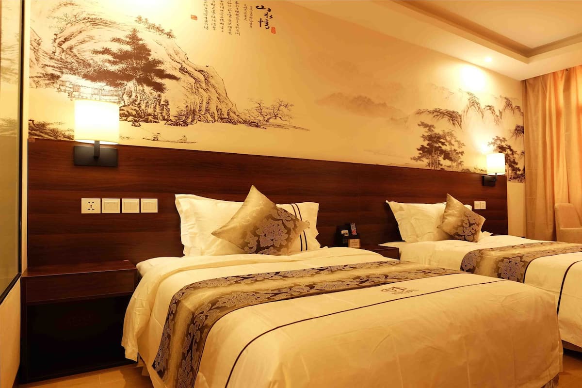 A hotel room with two beds, a wooden headboard, a wall mural, and a curtain.